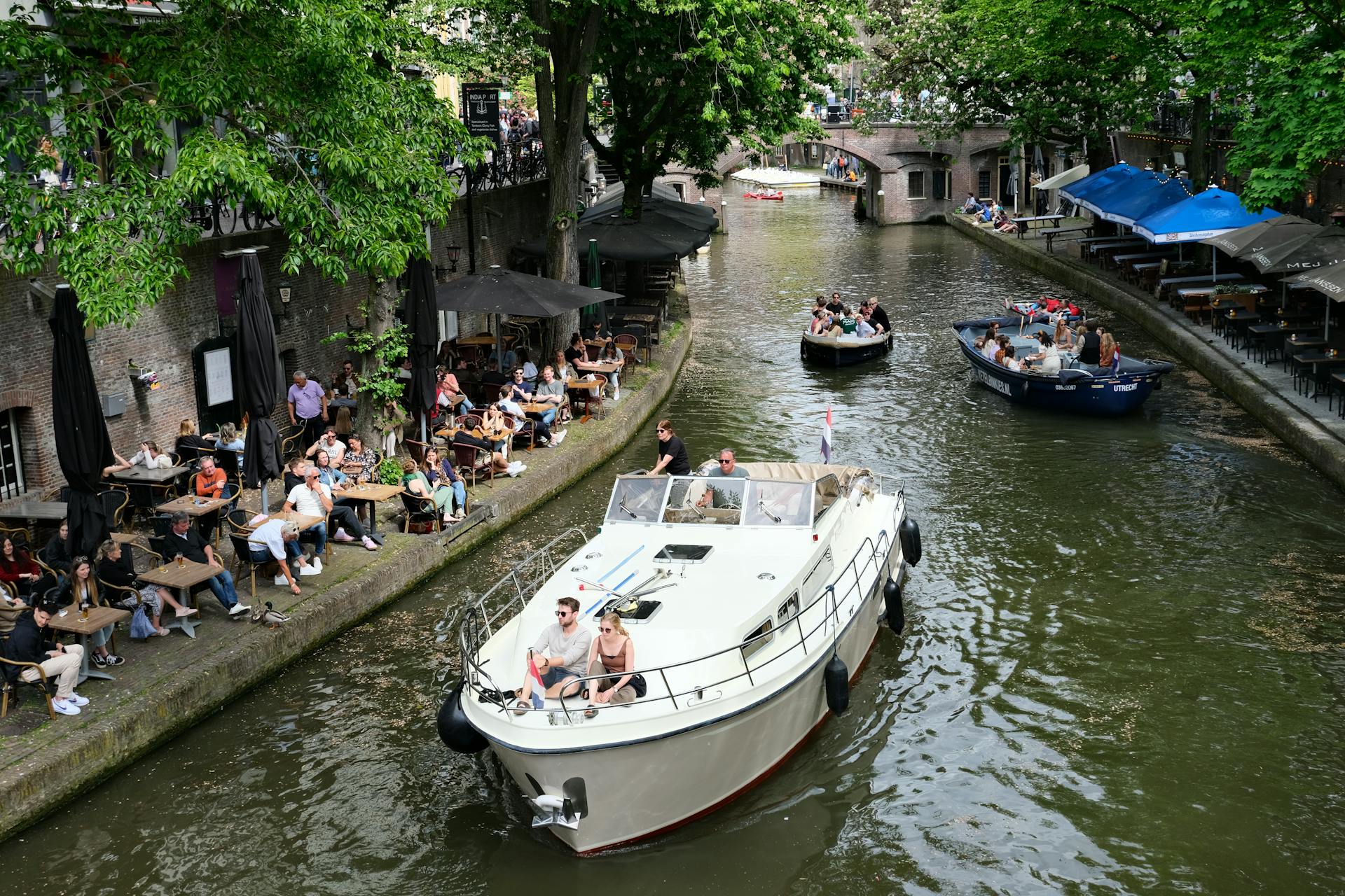 Vibrant scene of boats navigating Utrecht canal, flanked by bustling cafes.