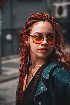 Stylish redhead with curly hair and denim jacket, posing in an urban environment.