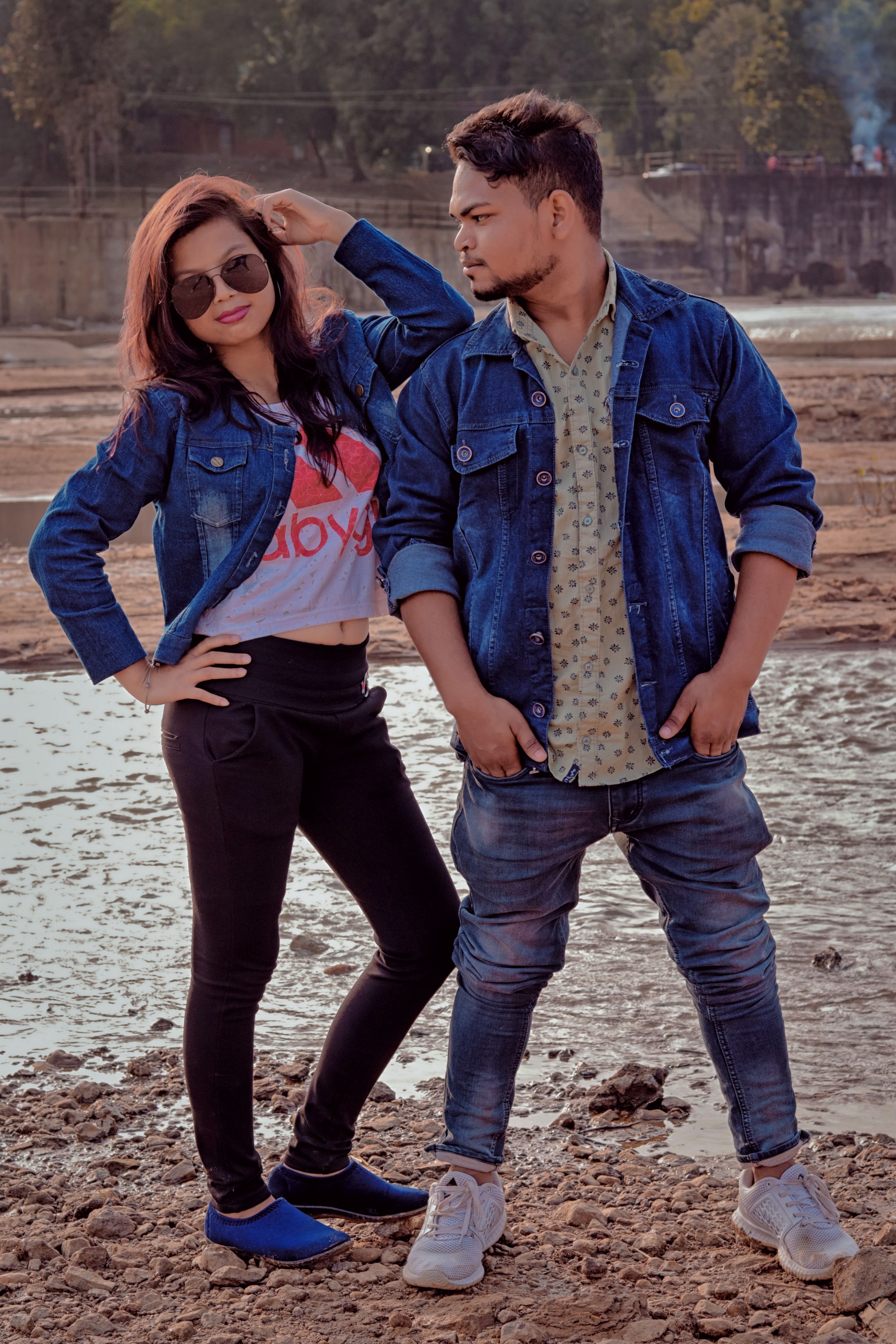 Stylish young couple striking a pose by the beach in casual denim attire.