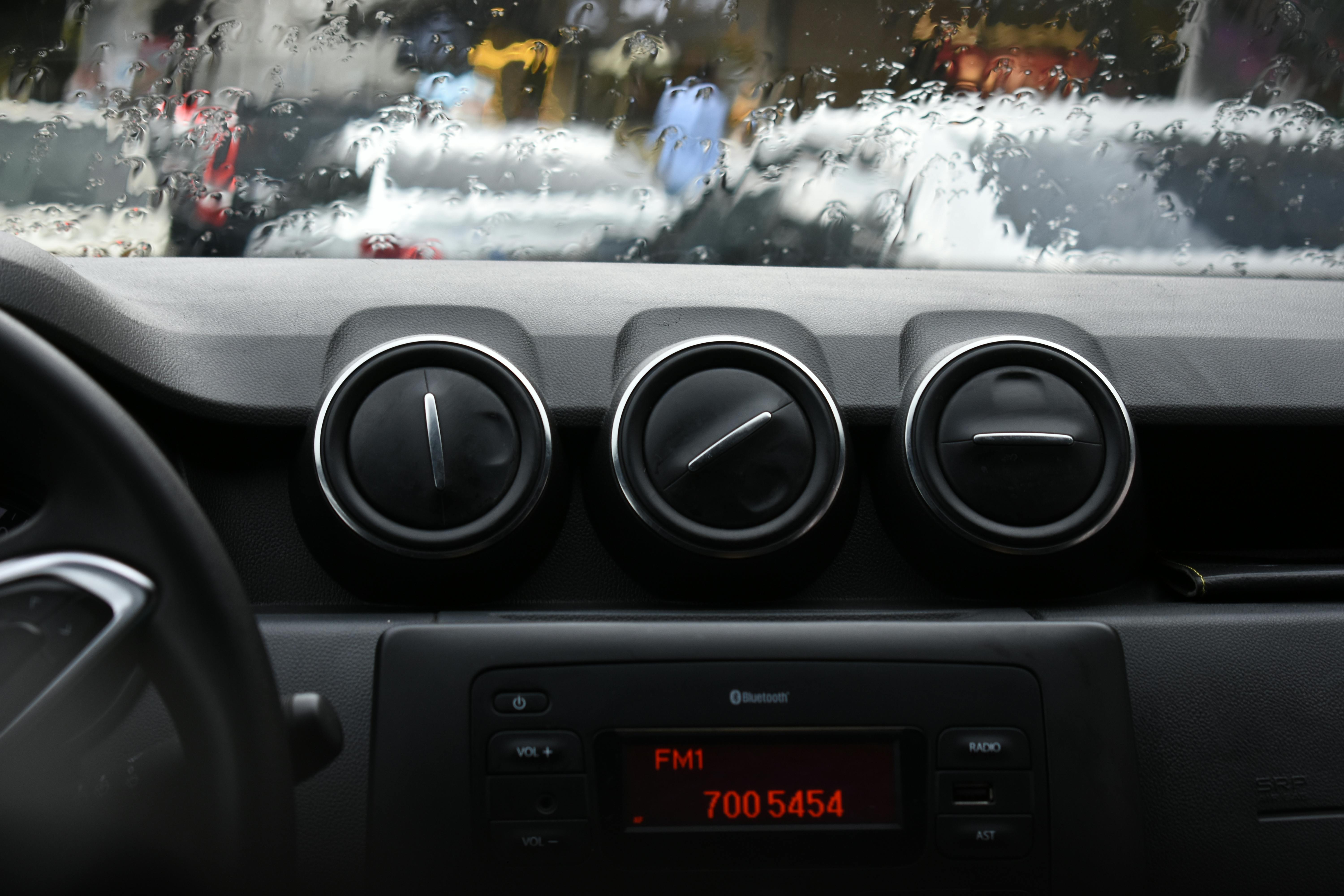 Close-up of a car dashboard and vents with raindrops on windshield, evoking a cozy vibe.