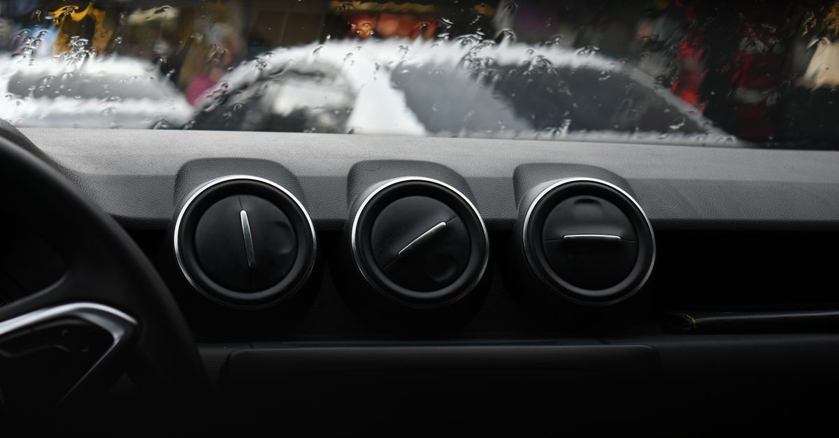 Close-up of car dashboard ventilation vents with a rainy windshield background.