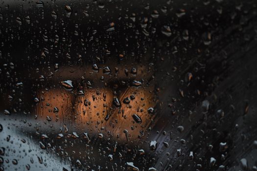 Close-up of rain droplets on a car window reflecting warm street lights at night.