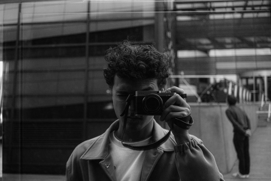 Black and white self-portrait of a photographer reflecting in a city window.