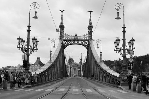 Monochrome view of Liberty Bridge in Budapest, hung with ornate street lights and bustling with people.