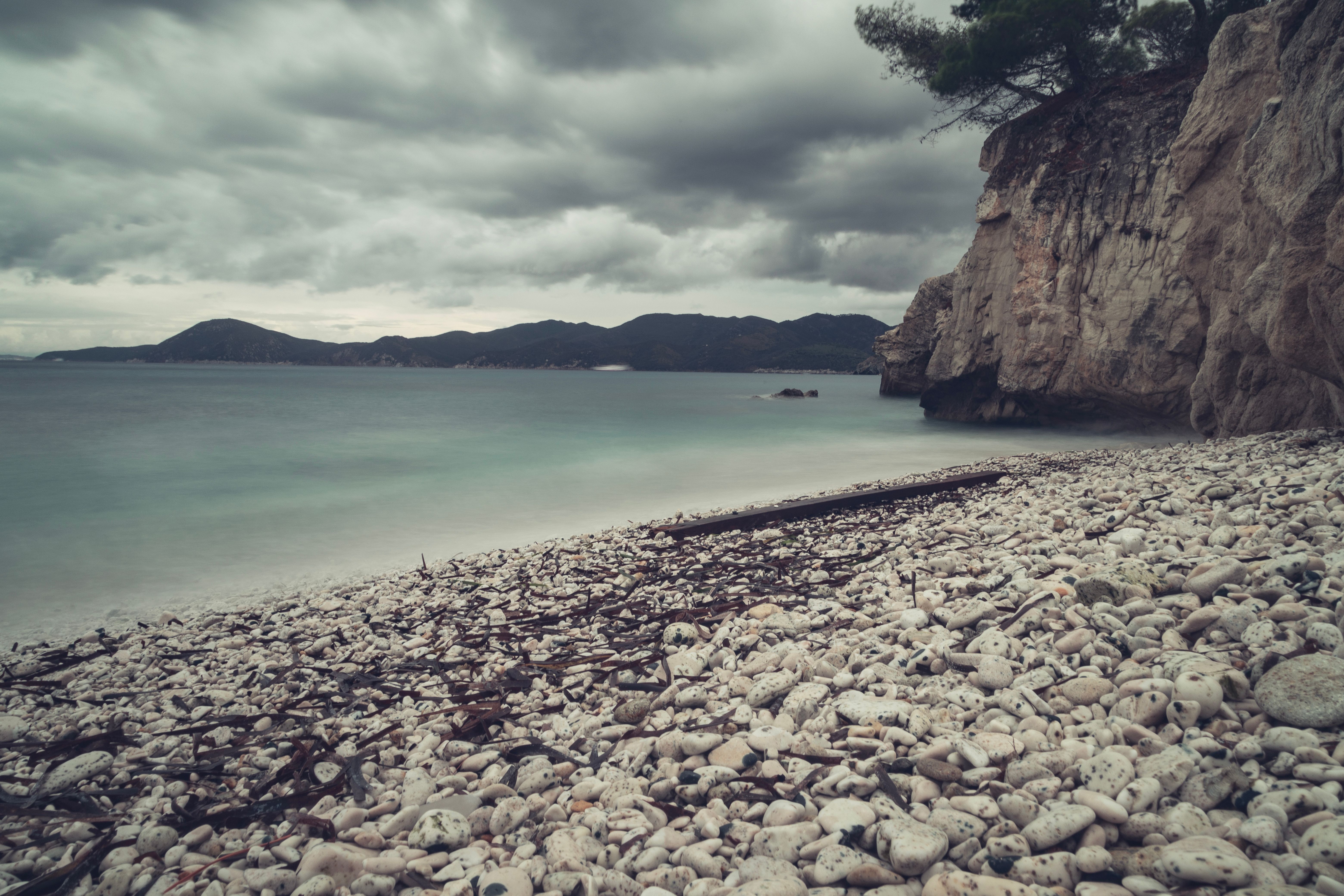 A beach with rocks and water under a cloudy sky · Free Stock Photo
