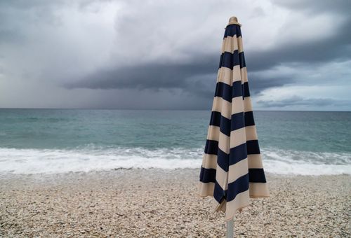 Free A closed striped umbrella on a pebble beach in Portoferraio, Italy with a stormy sky and sea. Stock Photo