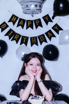 Smiling woman at a birthday celebration surrounded by black and white balloons and a cake.