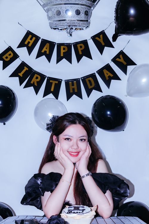 Free Smiling woman at a birthday celebration surrounded by black and white balloons and a cake. Stock Photo