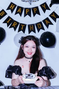 Young woman celebrating birthday with cake at festive party setup under 'Happy Birthday' banner.