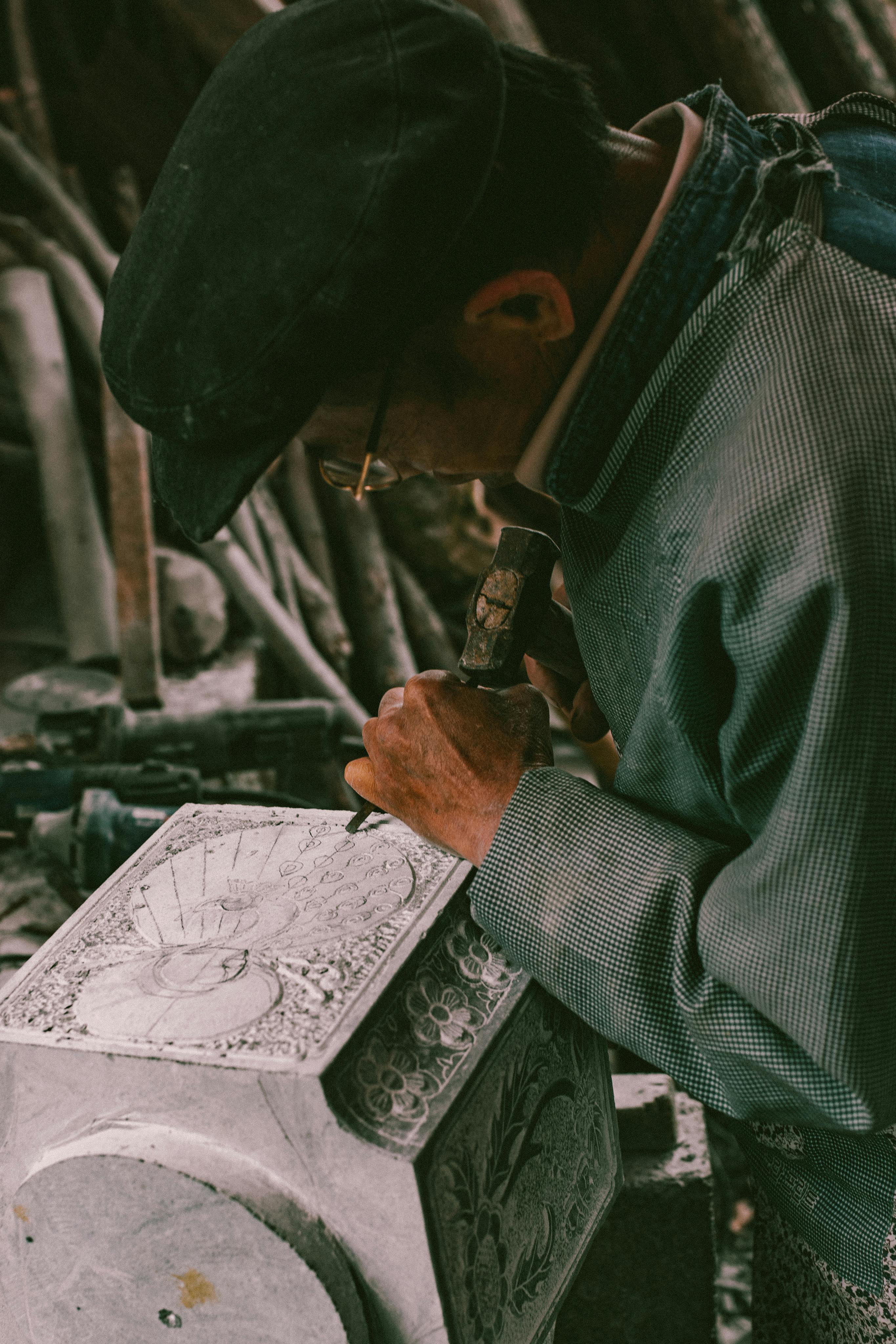 Elderly craftsman chiseling intricate designs on stone, showcasing traditional artistry.