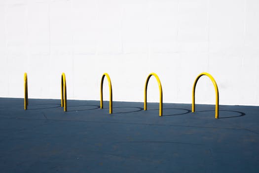 Photo by Athena Sandrini A minimalist image featuring yellow bike racks casting shadows on a blue surface against a white wall.