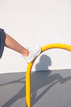 强光下，一只穿着白色运动鞋的脚在黄色栏杆上保持平衡，投下阴影的特写