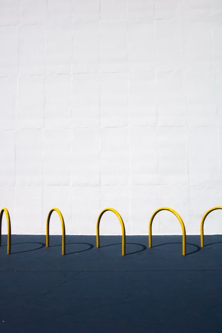 Modern minimalist photo of yellow bike racks casting shadows on a blue surface against a white wall.