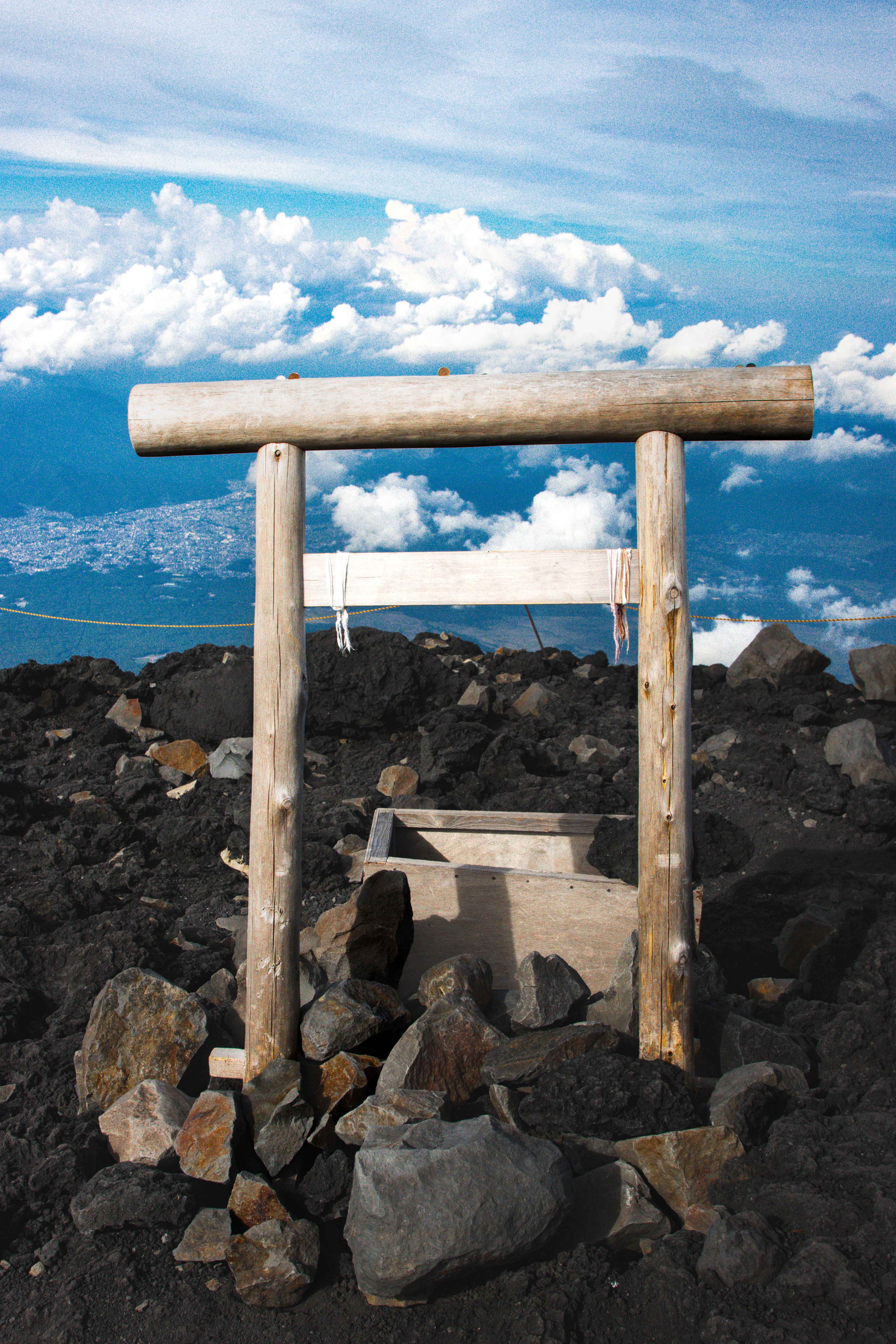 Wooden Torii gate at Mount Fuji summit with clouds and rocky terrain.