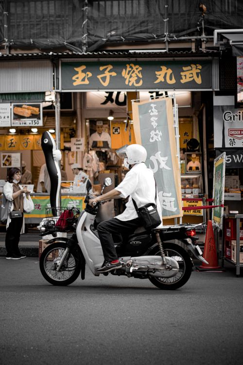 Free A man rides a scooter past a bustling urban storefront, capturing city life. Stock Photo