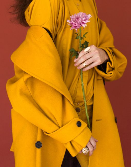 Chic woman in yellow coat holding a pink chrysanthemum on a red background.