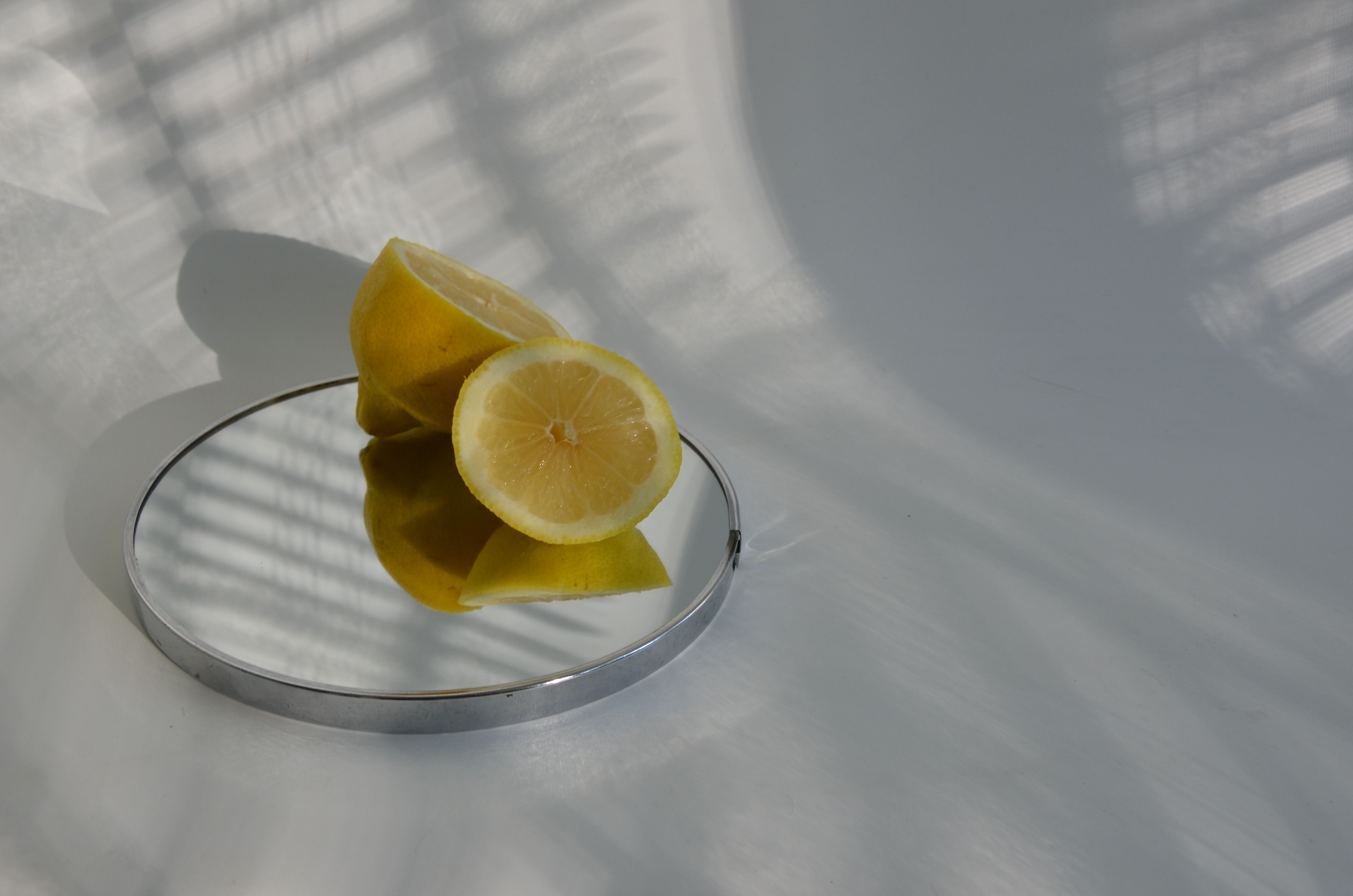 Sliced lemons on a mirror casting shadows, showcasing minimalistic food photography.