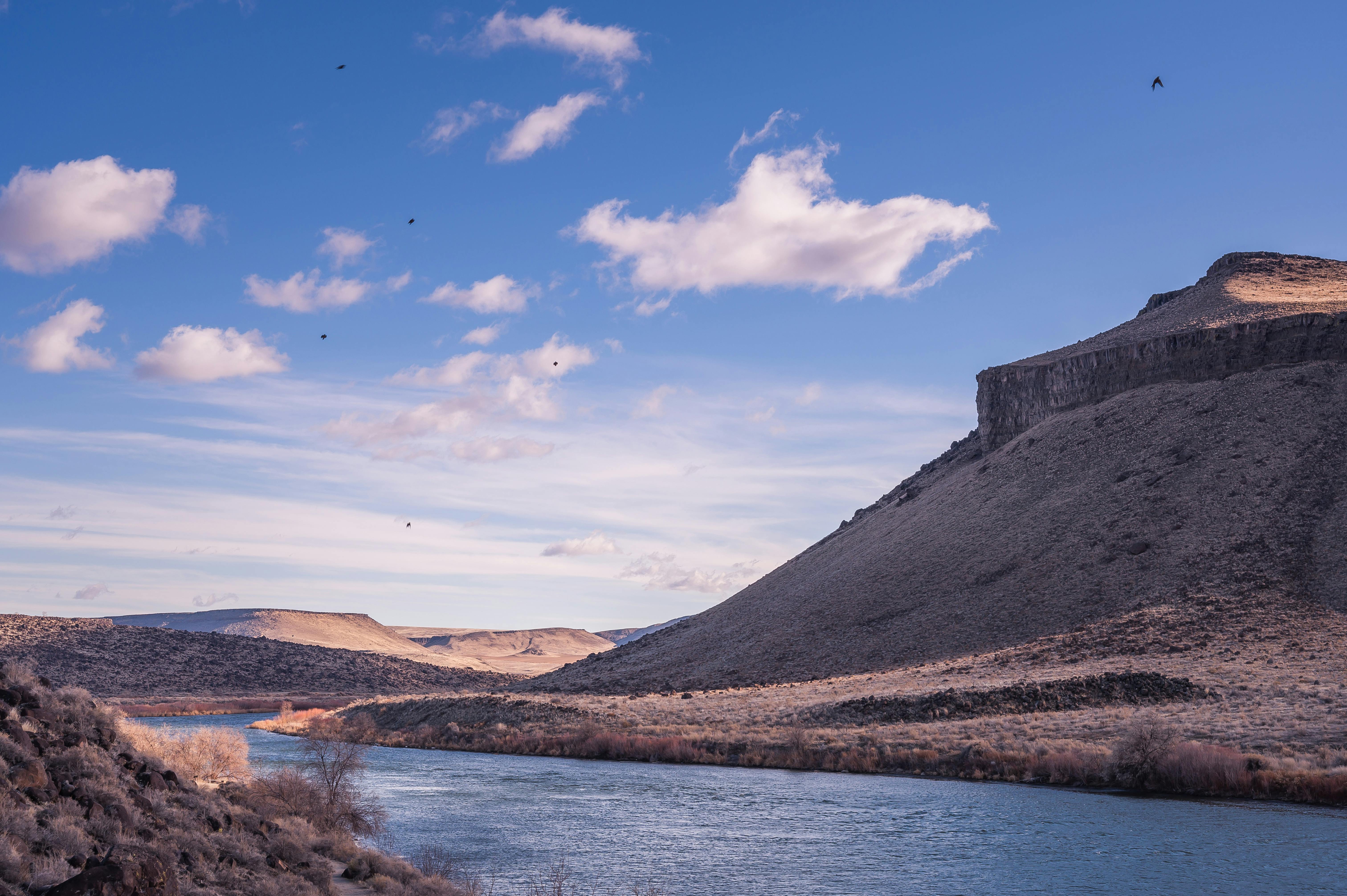 一条宁静的河流流过崎岖的山地，天空湛蓝，云层疏朗