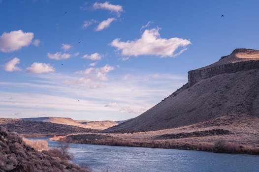 一条宁静的河流流过崎岖的山地，天空湛蓝，云层疏朗