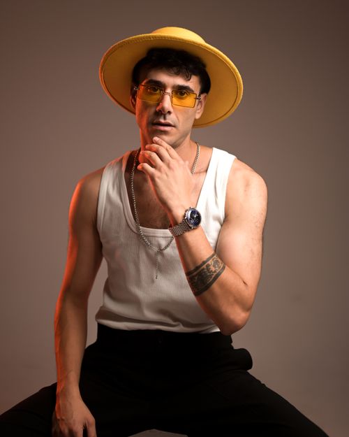 Free A fashionable man poses in a studio wearing a yellow hat, sunglasses, and modern attire. Stock Photo