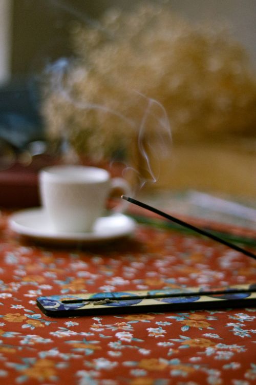Free Incense smoke rises beside a cup on a floral-patterned background, creating a serene vibe. Stock Photo