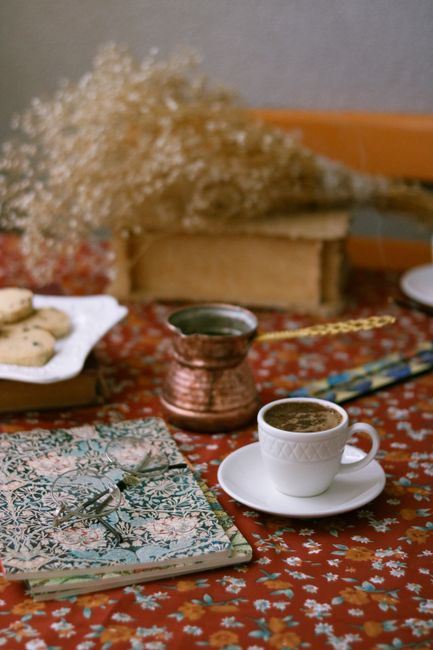 A warm still life featuring coffee, cookies, and a notebook on a floral tablecloth.