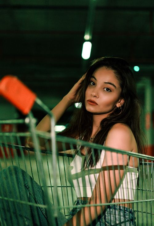 Free Stylish portrait of a young woman sitting in a shopping cart, depicting modern urban fashion. Stock Photo