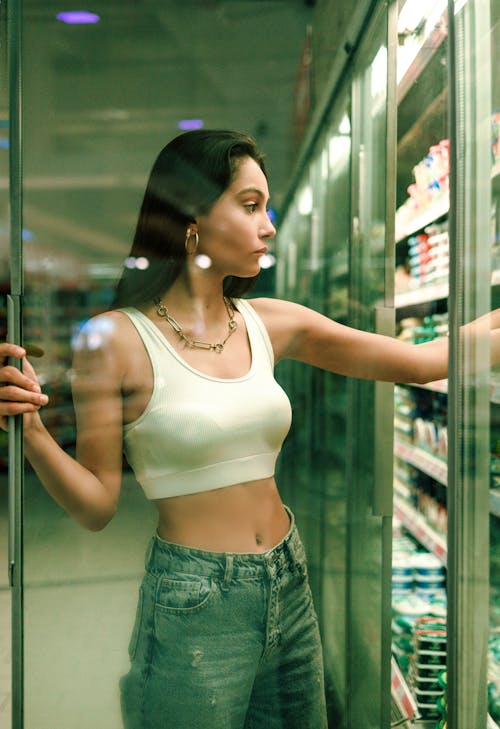 A woman in a white top and jeans standing in front of a refrigerator