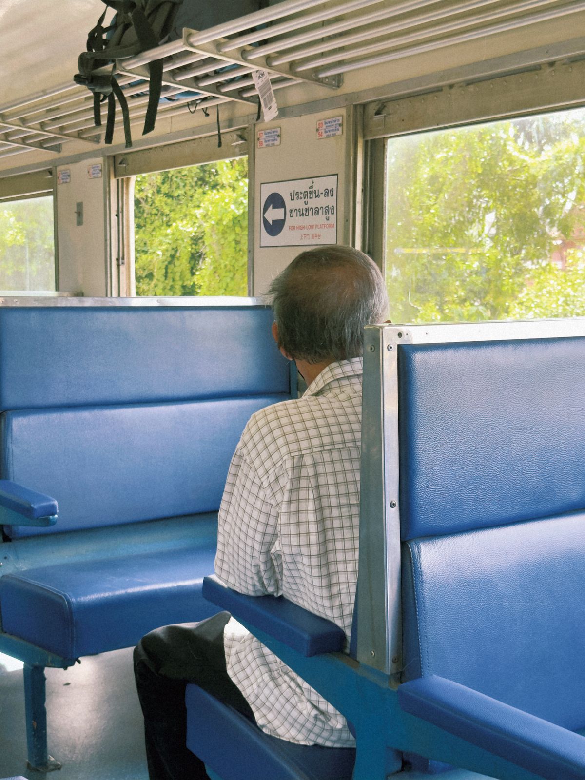 An elderly man sitting on a blue train seat looking out the window during his journey