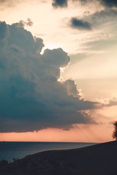 Serene ocean view with dramatic clouds at sunset, creating a stunning silhouette and warm glow.