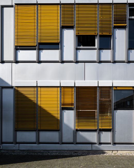 Close-up of an urban building facade in Berlin featuring yellow blinds and reflective windows.