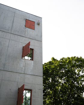 Concrete building with red windows next to green trees, showcasing urban architecture.