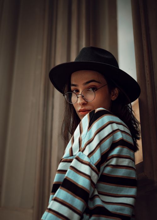 Free Woman in glasses and hat posing indoors with striped sweater, evoking a retro fashion vibe. Stock Photo