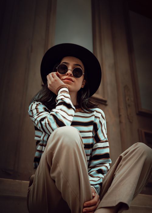 Free Fashionable portrait of a woman in sunglasses and a hat, sitting confidently outdoors. Stock Photo
