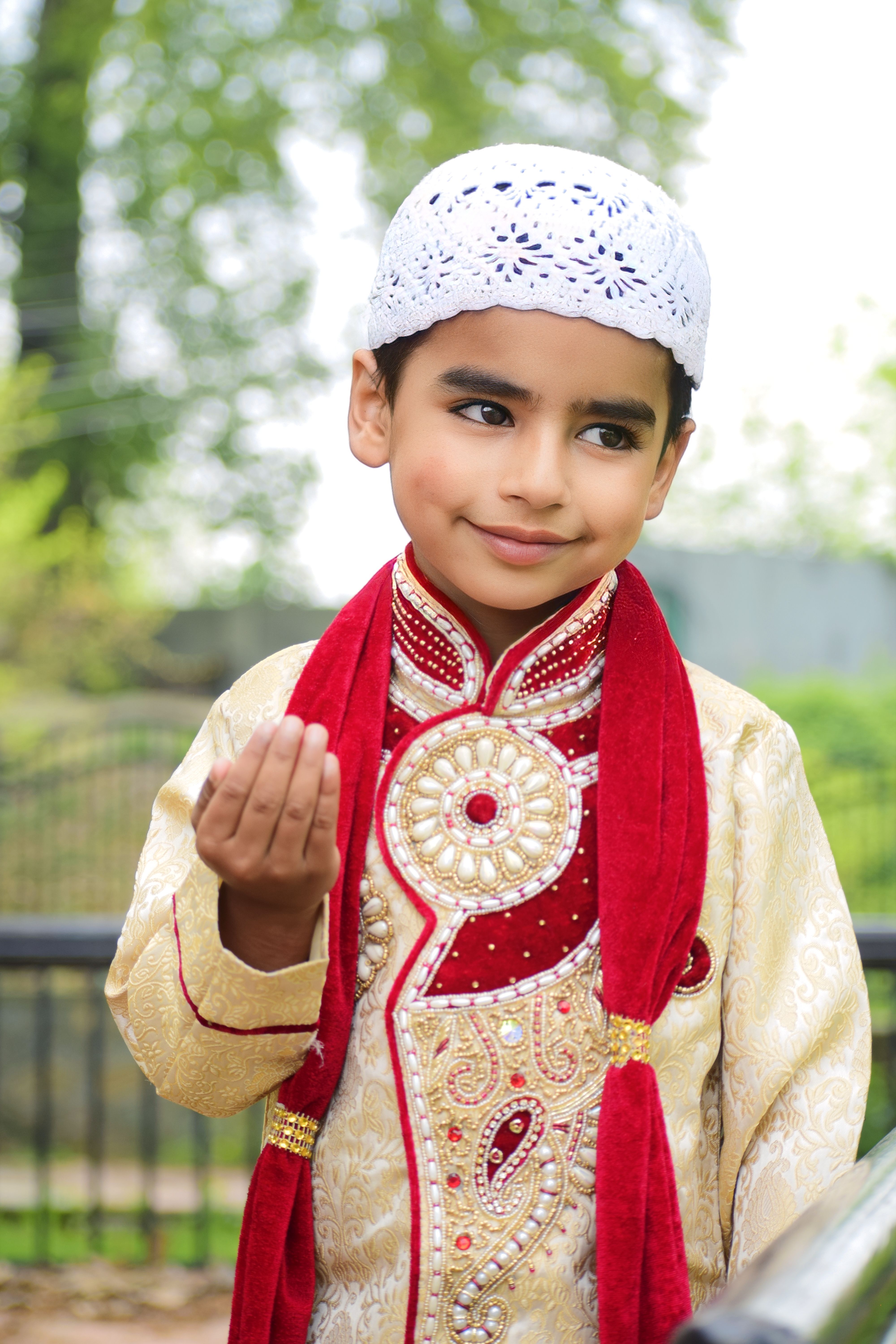 Charming portrait of a young boy in traditional attire with ornate embroidery and a welcoming gesture.