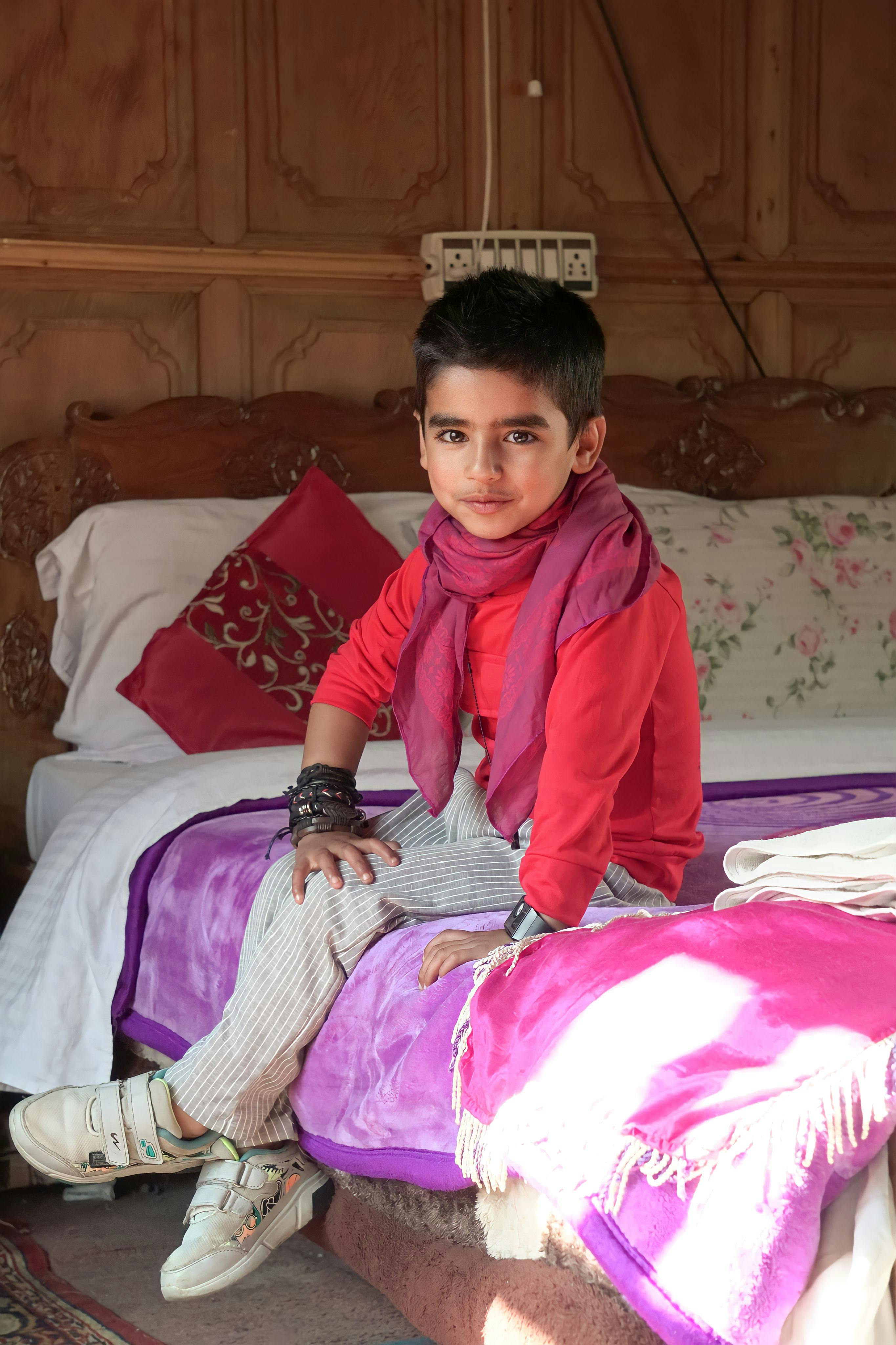 A young boy wearing a red sweater and scarf poses confidently in a colorful room setting, capturing the essence of childhood fashion.
