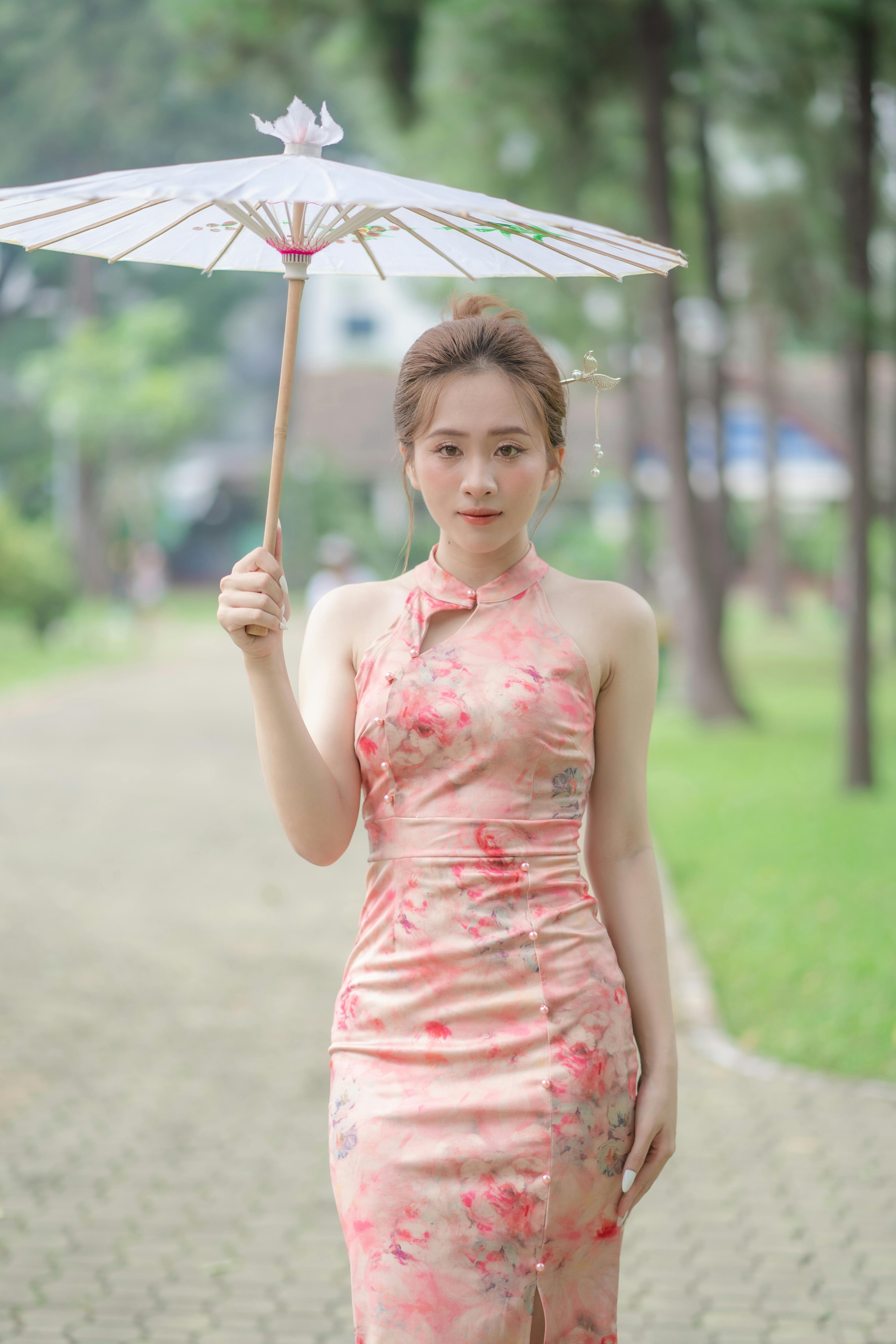 A young woman poses gracefully in a park, wearing a floral qipao with a paper umbrella.