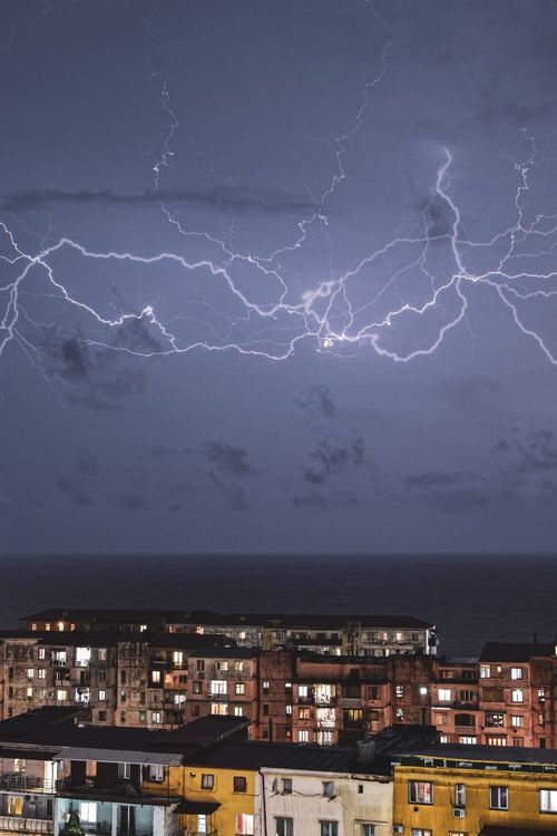 Free Striking lightning across a city skyline by the sea during a powerful thunderstorm. Stock Photo