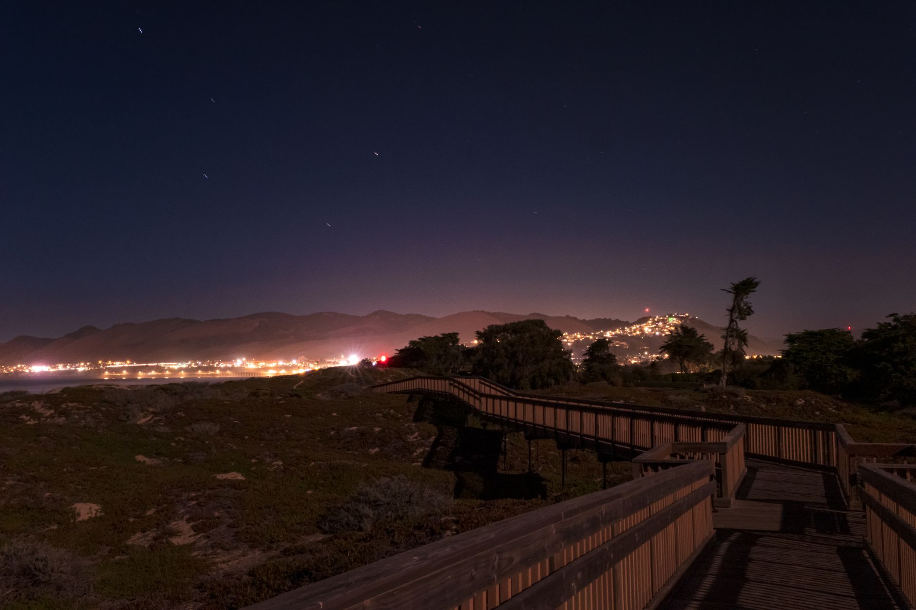 Nighttime view of Pismo Beach boardwalk with city lights and clear sky.