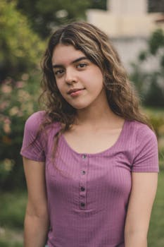 Outdoor portrait of a young woman in a purple top with curly brown hair.