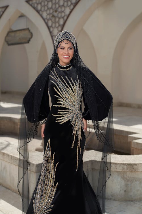 Elegant Woman in a Black Dress and a Headdress Standing near a Building