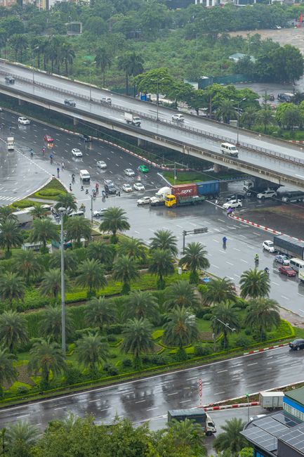 Photo by HONG SON A rainy urban scene with traffic, palm trees, and a highway overpass captured from above.