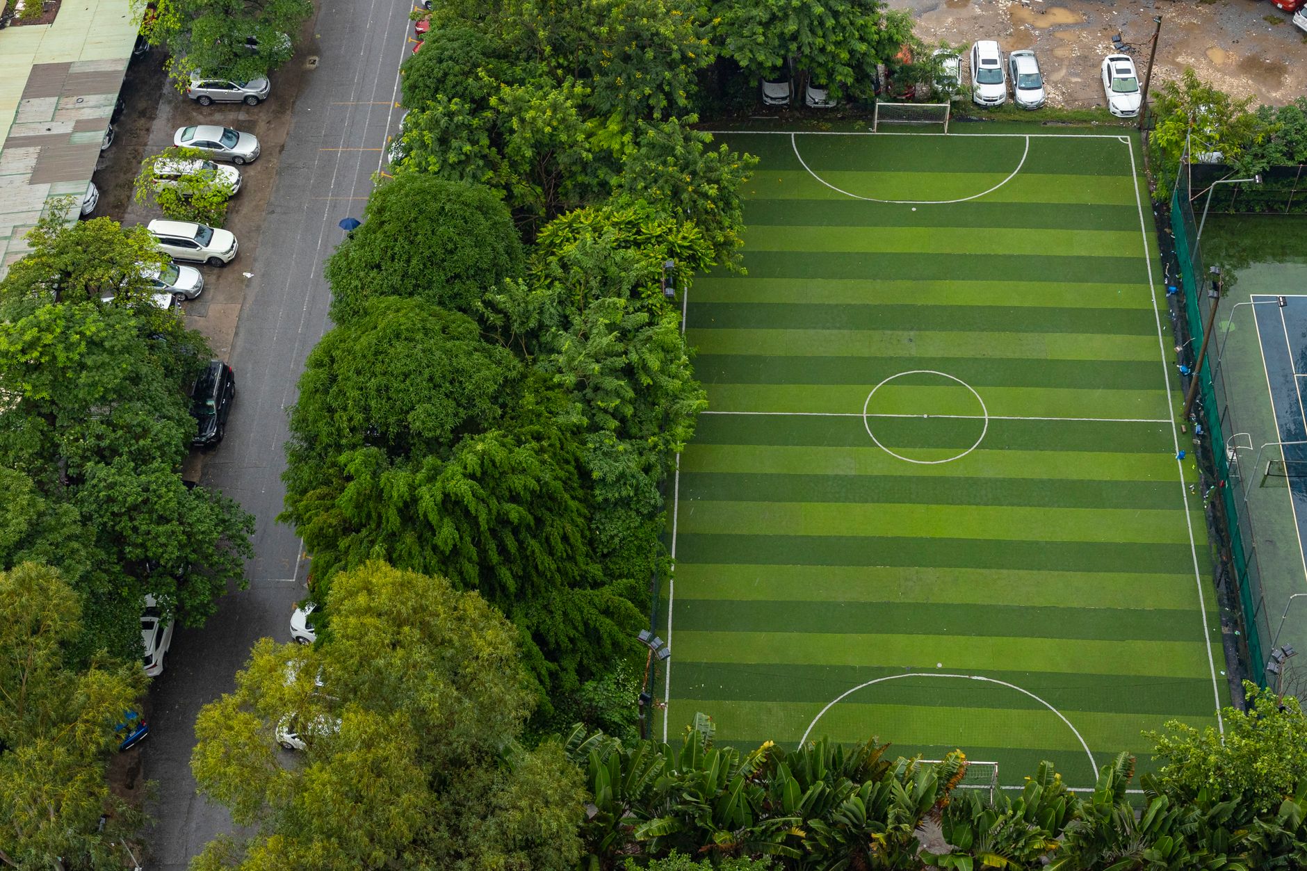 Aerial view of a soccer field surrounded by trees and a nearby parking area.