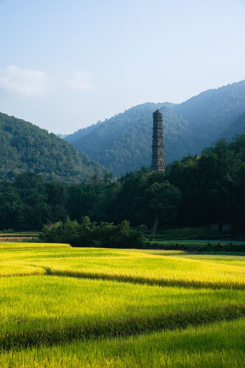 Free A serene view of a tall tower surrounded by vibrant green fields and forested mountains. Stock Photo