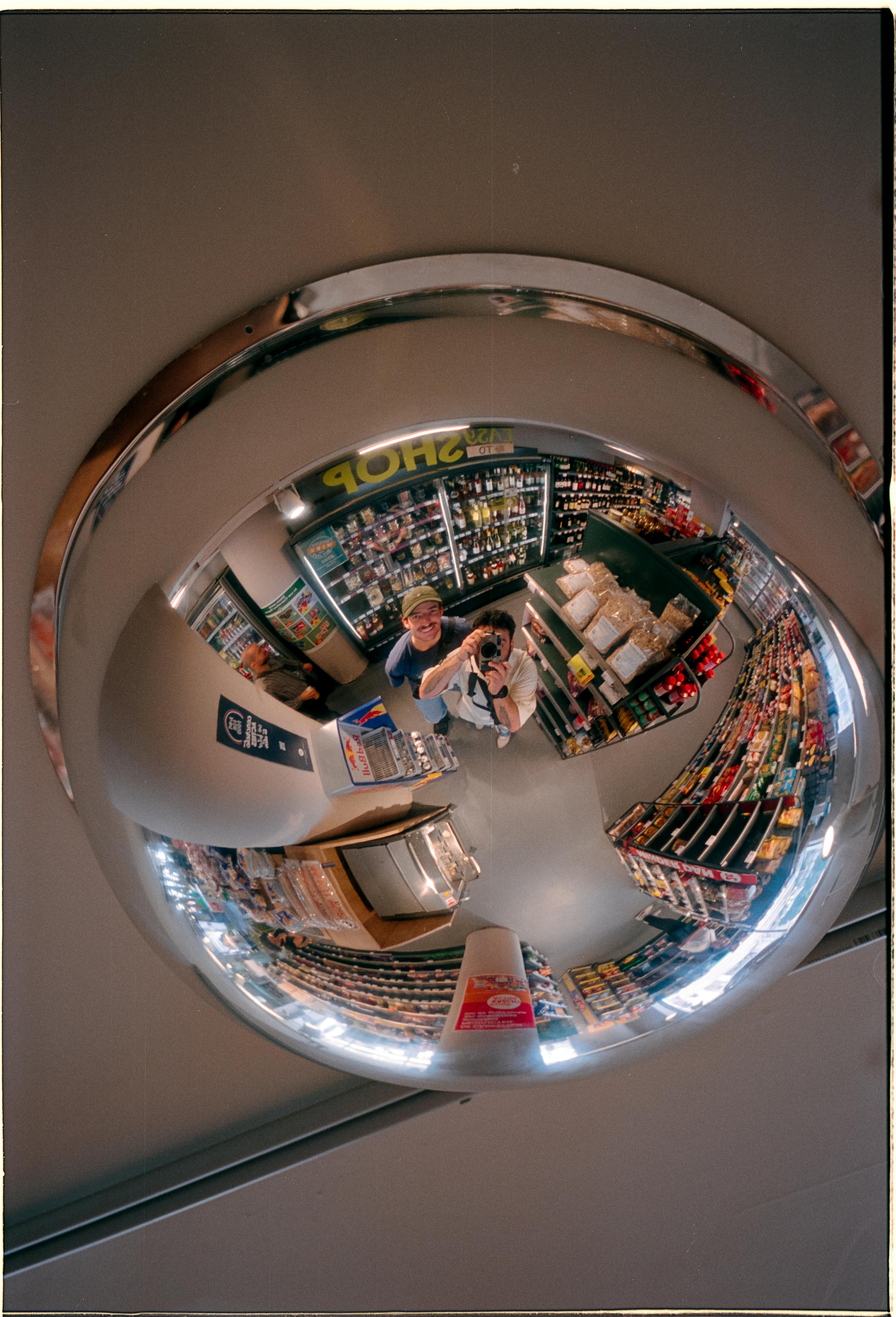 Fisheye mirror reflection capturing a supermarket aisle filled with various products and a visible photographer.