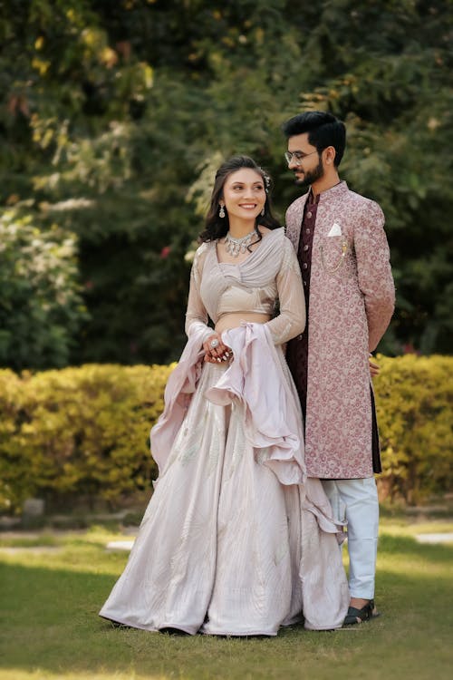 Bride and Groom in Traditional Wedding Clothing Standing in a Garden and Smiling 