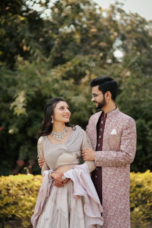 Bride and Groom in Traditional Wedding Clothing Standing in a Garden and Smiling 