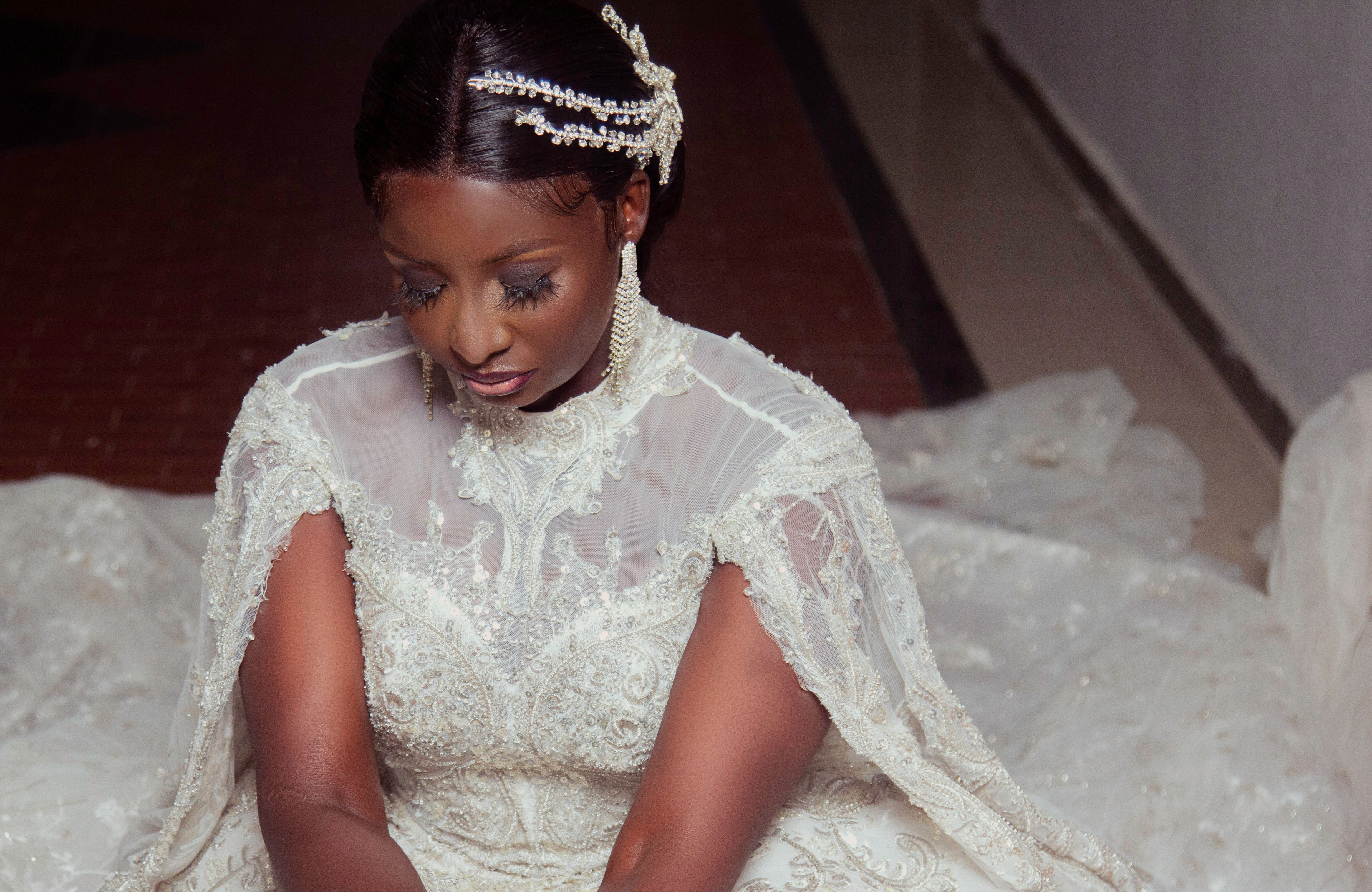 Beautiful bride in an intricate lace wedding dress, adorned with pearls and jewelry, captured indoors.