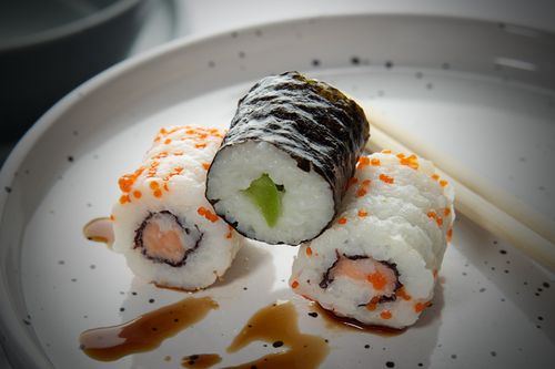 Free Delicious sushi rolls of salmon and avocado garnished on a speckled ceramic plate with sauce. Stock Photo