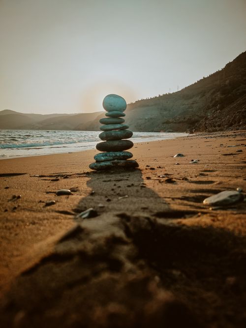 Free A tranquil beach scene featuring a cairn stacked on sandy shores with a sunset backdrop. Stock Photo